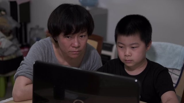 Chinese kid and mother doing online schooling at home amid coronavirus pandemic