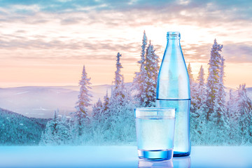 Mineral water bottle with glass on spectacular snow forest and mountains. Fresh natural water.