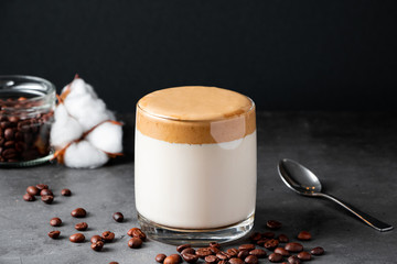 Dalgona coffee on a black background. Making a trendy drink. Fluffy sweet foam in a glass with iced milk.
