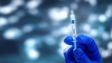 coronavirus covid-19 vaccine syringe in hand with medical blue glove with blurred bokeh background, coronavirus covid-19 vaccine development