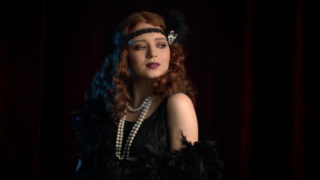 Portrait of old-fashioned red haired woman dressed in Roaring twenties era flirting and posing on burgundy velours background. Vintage, flapper party, retro fashion concept