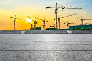 Empty square floor and construction site silhouette at sunrise.