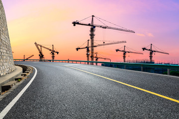 Fototapeta premium Empty asphalt road and construction site landscape at sunrise.