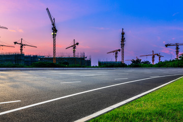 Empty asphalt road and construction site landscape at sunrise.