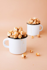Caramel popcorn in vintage white metal cups on a brown background