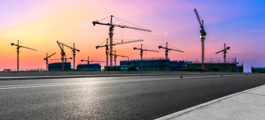 Empty asphalt road and construction site landscape at sunrise.