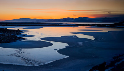 Dramatic sunset reflects orange color into tidal pools near black beach and Vestrahorn