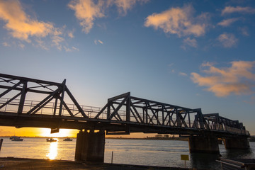 Fototapeta na wymiar Sun rises on horizon under Tauraga railway bridge.