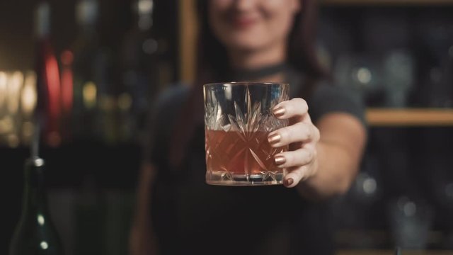 Attractive bartender holding mixed drink in crystal lowball glass, close.