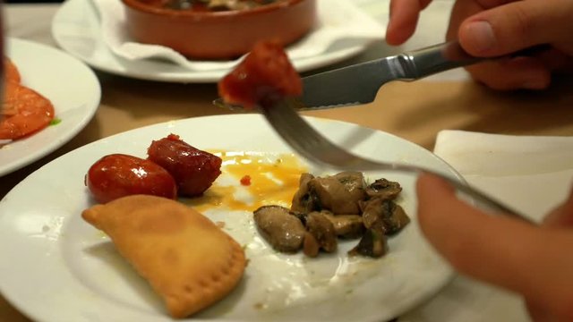 Person eating meal of sausage and mushrooms from the plate with fork and knife - Powered by Adobe