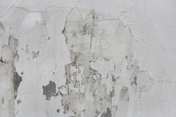 White dirty concrete wall with cracks and falling pieces of old white paint. Shabby white or gray  wall of abandoned building.