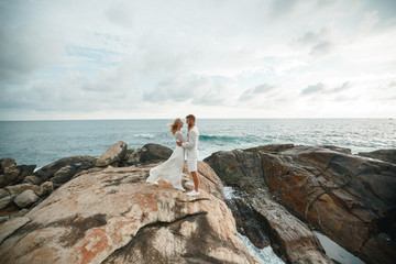 beautiful gorgeous bride and stylish groom on a romantic moment stands on a cliff above the sea