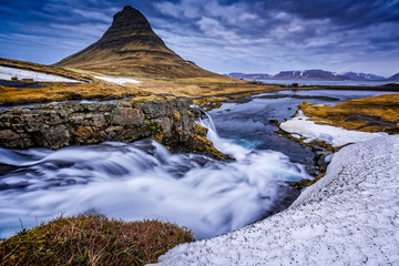 Mount Kirkjufell towers over rushing waterwalls in Iceland.