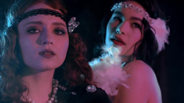 Attractive flappers women dressed in style of Roaring twenties posing on neon smoky background. Vintage, retro party, fashion, girls friends concept