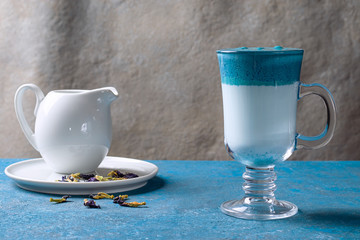 Dalgona Matcha Blue Latte, cream matcha in a glass cup on a blue background. Horizontal orientation