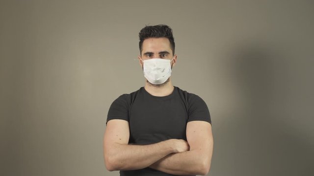 Young man with surgical Mask for coronavirus prevention, caucasian guy, crossing arms looking at camera in studio, during covid-19 pandemic in France. One person isolated. 4K UHD.