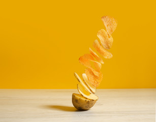Flying potato slice into potato chips isolated on yellow background