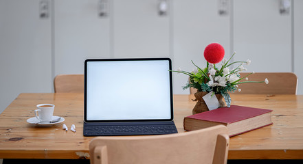 Tablet with keyboard on wooden table in co-workspace, blank screen for graphic design.