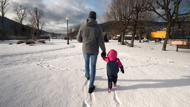 Father and child walking together outdoors on snowy winters day, rear view tracking