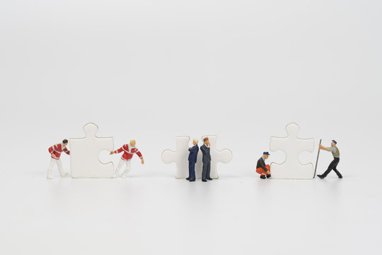 miniature people teamwork try to complete jigsaw puzzle on white background