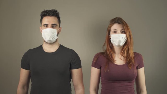 Isolated young couple with surgical Masks, standing and facing at camera in studio, during covid-19 pandemic virus in France. 4K UHD. Two persons. Disease Prevention. Social Distance in relationship.