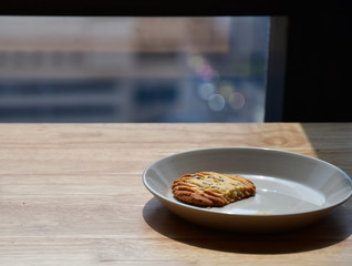 One healthy homemade cereal cookie that was left on a gray ceramic plate on a wooden table on the side of the window and exposed to sunlight.Delicious snacks that are eaten until only one piece remain