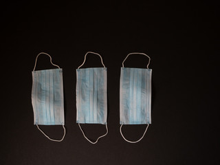 Three Disposable LIght Blue Face Masks on Black Background. Photographed with selective focus and copy space.