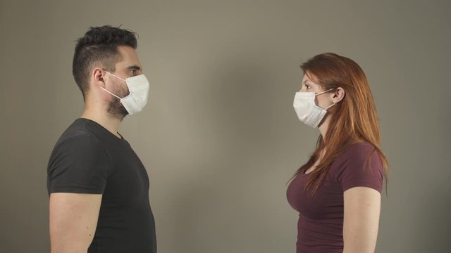 Isolated couple with surgical Mask, standing and facing in studio, during covid-19 pandemic virus in France. 4K UHD. Two young persons. Disease Prevention. Social Distance in relationship.
