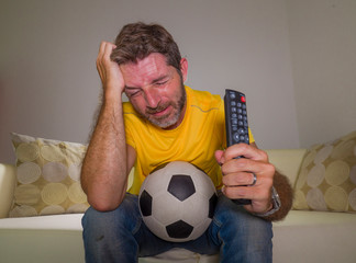 Fototapeta frustrated football fan in intense emotion - home portrait of young dejected and sad man watching soccer game on television at living room couch his team losing obraz