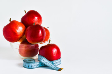 Beautiful juicy red apples in a transparent plate, and separately an apple with a measuring tape on a white background. Weight loss concept.