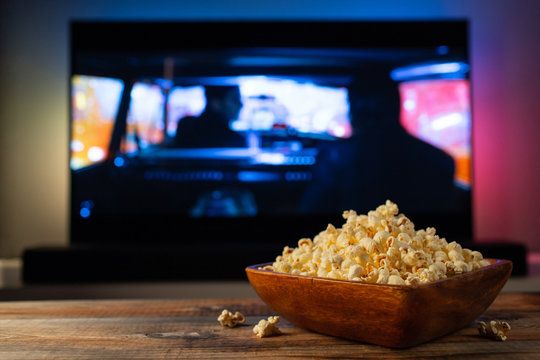 A Wooden Bowl Of Popcorn And Remote Control In The Background The TV Works. Evening Cozy Watching A Movie Or TV Series At Home