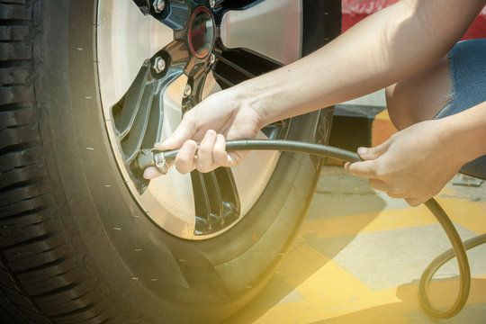 Asian woman driver checking air pressure filling air into a car tire to increase pressure car tire close up. The right tire pressure reduces accidents, increases safety.