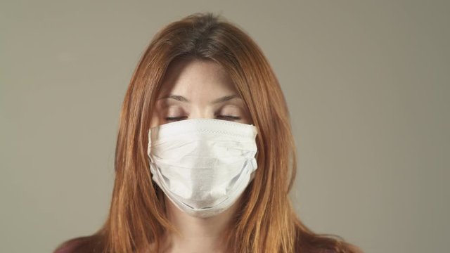 Close-up of Isolated caucasian woman with surgical Mask, red hair and shirt standing and facing at camera in studio, during covid-19 pandemic in France. 4K UHD. One person young girl turning head.