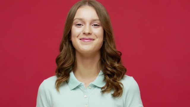 Cheerful brunette woman in polo t-shirt smiling playfully and flirting, moving impatiently, in anticipation of something pleasant, positive emotions. indoor studio shot isolated on red background