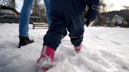 Baby legs following fathers footsteps, walking on snow, wintertime