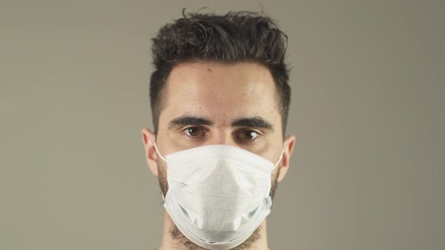 Isolated man with surgical Mask, brown hair and eyes, facing at camera in studio, during covid-19 pandemic virus in France. 4K UHD. Close-up of One person young man. Prevention.