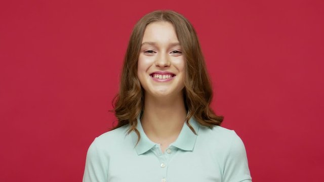 Playful happy carefree young woman in polo t-shirt grimacing and grinning, showing tongue out with disobedient naughty expression, aping and playing fool. indoor studio shot isolated on red background