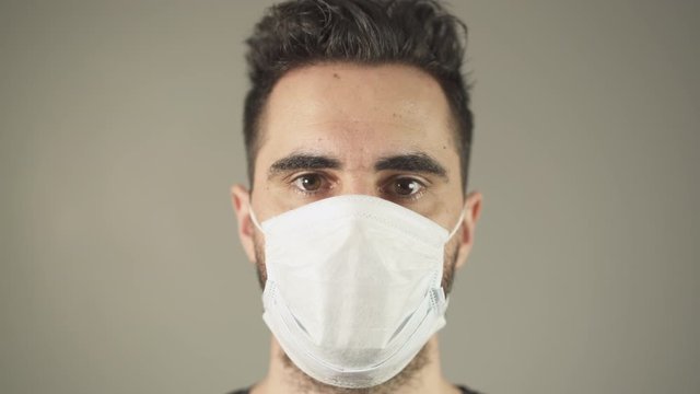 Close-up of Isolated man with surgical Mask, brown hair and eyes, facing at camera in studio, during covid-19 pandemic virus in France. 4K UHD. One person young man. Prevention.
