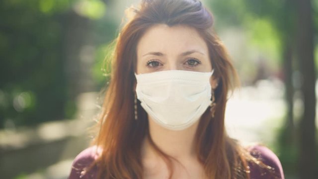Isolated Masked caucasian woman, redhead and freckles, red hair and shirt standing and facing at camera outside in street, during covid-19 pandemic in France. 4K UHD. One person young girl close-up.