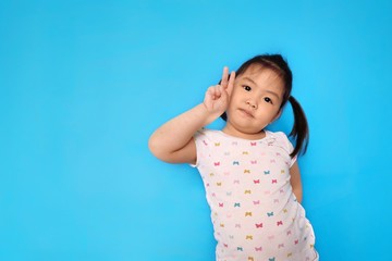 A cute young Asian girl is gesturing a victory sign using 2 fingers. Plain light blue background.