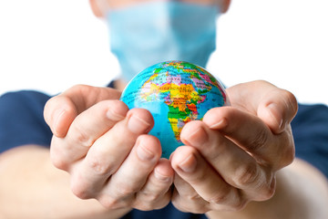 .Close-up of a man's hands holding a small globe, with images Africa,   a man in a medical mask out of focus, dressed in a blue t-shirt, uniform on a white isolated background.  Coronavirus, Covid-19