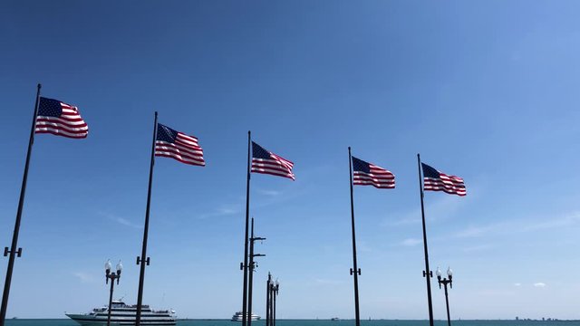 Shot of five American flags in the navy pier of Chicago. Five flags of the United States of America waving in a blue sky. Flag of EUA waving in Illinois, with a ship in the background.
