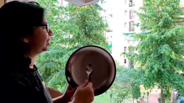 Young Indian girl making noise with a plate and spoon as a mark of respect for essentia l healthcare workers, medical personel, doctors, policemen and more during the coronavirus lockdown in India