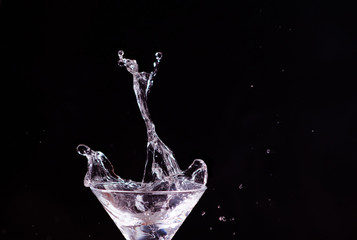 Splashes fly out of a martini glass on a black background
