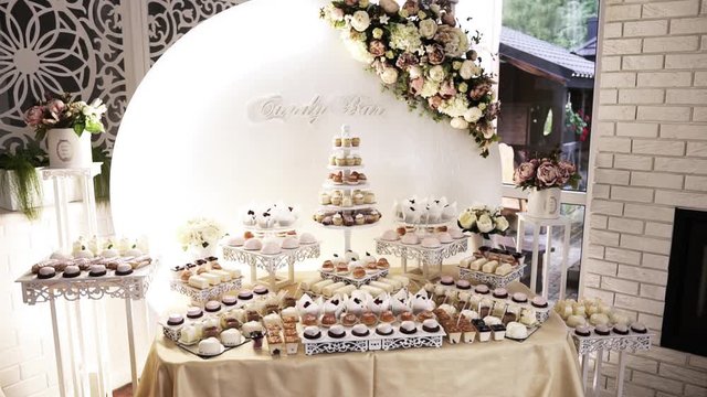 A large, beautiful, bright buffet with many sweet snacks, a candy bar, is on a white table and is waiting for guests at the celebration.