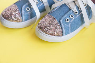 Fototapeta na wymiar Fashionable blue sneakers for girls isolated on yellow background. Pair of trendy kids sports shoes.Trandy denim sneakers for kids.Pair of trendy shiny sneakers, with white laces. Youth style