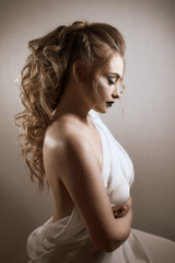 tanned girl with black lips and arrows with light curly hair and professional bright makeup, isolates on white in a silk white dress
