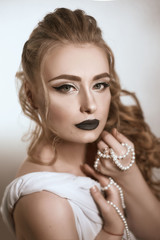 Obraz premium tanned girl with black lips and arrows with light curly hair and professional bright makeup, isolates on white in a silk white dress