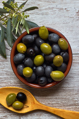 Clay bowl with black and green olives, a wooden spoon and olive branch