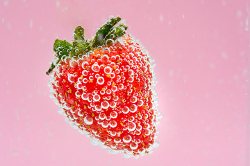 Red strawberry fruit floating in the water on pink background. High value commercial food photography. Fresh beverage drink concept.